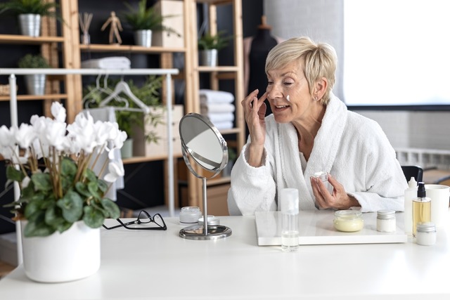 Seniorin cremt sich ein im Bademantel.